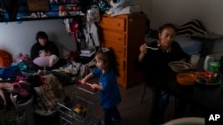 Deneffy Sánchez, left, looks at his smartphone on a bunk bed he shares with his mother, Lilian Lopez, right, and sister, Jennifer, in a shared studio apartment in Los Angeles, Saturday, Sept. 9, 2023. (AP Photo/Jae C. Hong)