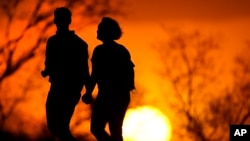 In this file photo, a couple walks through a park at sunset, March 10, 2021, in Kansas City, Mo. (AP Photo/Charlie Riedel, File)