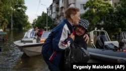 FILE - A volunteer carries a woman as she is evacuated from a flooded Kardashynka village of the bank Dnipro river, in Kherson, Ukraine on June 9, 2023. (AP Photo/Evgeniy Maloletka)