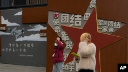 两个年轻人走过北京街头一堵政府的宣传墙。（2024年1月17日）