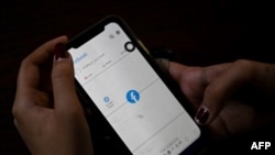 မိုဘိုင်းဖုန်းနဲ့ Facebook အသုံးပြုနေသူတဦး (ဓါတ်ပုံ-AFP)