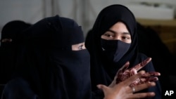 A veiled Indian Muslim student, her hands decorated with henna, talks to her friend as they gather to meet student activists in Kundapur in district Udupi, Karnataka state, India, Saturday, Feb. 26, 2022. (AP Photo/Aijaz Rahi)
