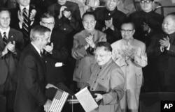 1979年8月28日，美国副总统蒙代尔和中国副总理邓小平在两国文化和水电协议书签署后，交换协议文本。前排鼓掌者有中国总理华国锋（中）、美国驻华大使伦纳德•伍德科克（华国锋左侧）和中国外交部长黄华（华国锋右侧）