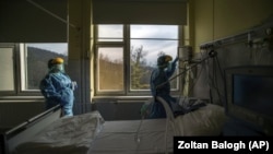 In this March 24, 2020, file photo, medical staff members check a ventilator in protective suits at the care unit for the new COVID-19 infected patients inside the Koranyi National Institute of Pulmonology in Budapest. (Zoltan Balogh/MTI via AP, File)