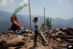 In this April 8, 2016 photo, Khendo Tamang, 8, stands near the debris of the collapsed home she was trapped in after the April 25, 2015 earthquake struck in Banskharka, Nepal.