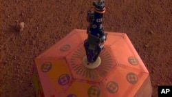 This photo provided by NASA Jet Propulsion Laboratory, shows the Mars InSight lander placing a quake monitor on the planet’s dusty red surface. InSight’s robotic arm removed the seismometer from the spacecraft deck and set it directly on the ground Wedne