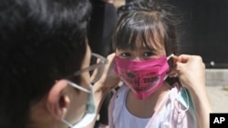 FILE - In this June 10, 2020, file photo, Olivia Chan's father helps her with a new mask she received during a graduation ceremony for her Pre-K class in front of Bradford School in Jersey City, N.J. (AP Photo/Seth Wenig, File)