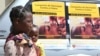 Une femme et son bébé passent devant les affiches de la campagne de vaccination contre le choléra dans un camp de déplacés à Beira, au Mozambique, le 3 avril 2019. 