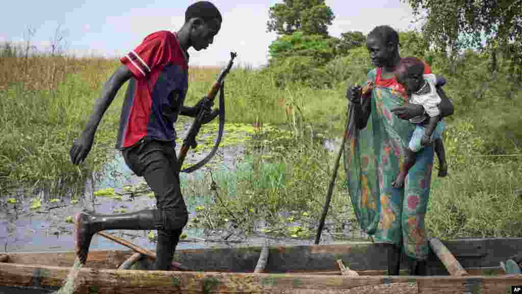 Une femme et un enfant de l&rsquo;ethnie Nuer et un rebelle montent sur une pirogue au milieu des marécages, près d&rsquo;un camp des déplacés inondé à Bentiu, Soudan du Sud, 20 septembre 2014. (AP Photo/Matthew Abbott)