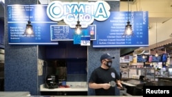 Athens Voulgaridis, owner of Olympia Gyro, serves customers at Reading Terminal Market that has seen reduced foot traffic due to the coronavirus disease (COVID-19) outbreak in Philadelphia, Pennsylvania, U.S., February 20, 2021. (REUTERS/Hannah Beier)
