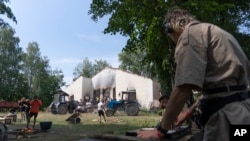 A music DJ at work while young volunteers clear debris from a building destroyed by a Russian rocket in the village of Yahidne, Ukraine, July 24, 2022. (AP Photo/Roman Hrytsyna)