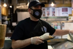 Athens Voulgaridis, owner of Olympia Gyro, serves customers at Reading Terminal Market that has seen reduced foot traffic due to the coronavirus disease (COVID-19) outbreak in Philadelphia, Pennsylvania, U.S., February 20, 2021. (REUTERS/Hannah Beier)