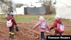 Des enfants syriens déplacés marchent dans la boue près de tentes dans un camp au nord d'Alep, près de la frontière avec la Turquie.