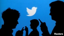 FILE - People holding mobile phones are silhouetted against a backdrop projected with the Twitter logo in this illustration.