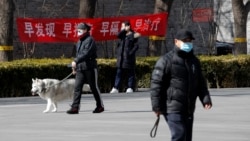 Residents wearing protective face masks walk by a propaganda banner which reads "Early detection, early reporting, early isolation and get early treatment" hangs on a neighborhood alley following the coronavirus outbreak in Beijing, Sunday, March 1, 2020.