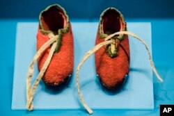 Photo shows a newborn's shoes made from a British red coat brought back at the end of the Revolutionary War