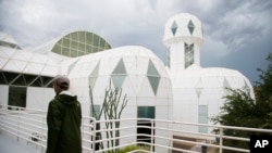 In this July 31, 2015 photo, a tourist walks to the main entrance of the Biosphere 2 facility while on a walking tour in Oracle, Ariz. (AP Photo/Ross D. Franklin)