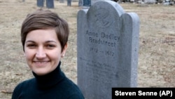 In this Tuesday, March 19, 2019, photo, Christy Pottroff, assistant professor of English at Merrimack College, kneels for a photograph near a commemorative marker, right, for 17th-century American poet Anne Bradstreet.