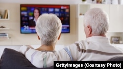 An older couple watching television in living room.