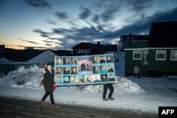 2025년 3월 11일 그린란드 누크에서 열린 그린란드에서 총선에서 한 남성이 옌스-프레데리크 니엘센 민주당 대표 등의 사진이 민주당 대형 포스터를 들고 투표소 앞을 지나고 있다.