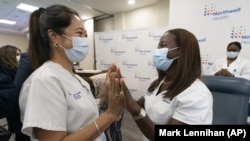 Nurse Annabelle Jimenez, left, congratulates nurse Sandra Lindsay after she is inoculated with the Pfizer-BioNTech COVID-19 vaccine, Monday, Dec. 14, 2020, at the Jewish Medical Center, in the Queens borough of New York. (AP Photo/Mark Lennihan, Pool)